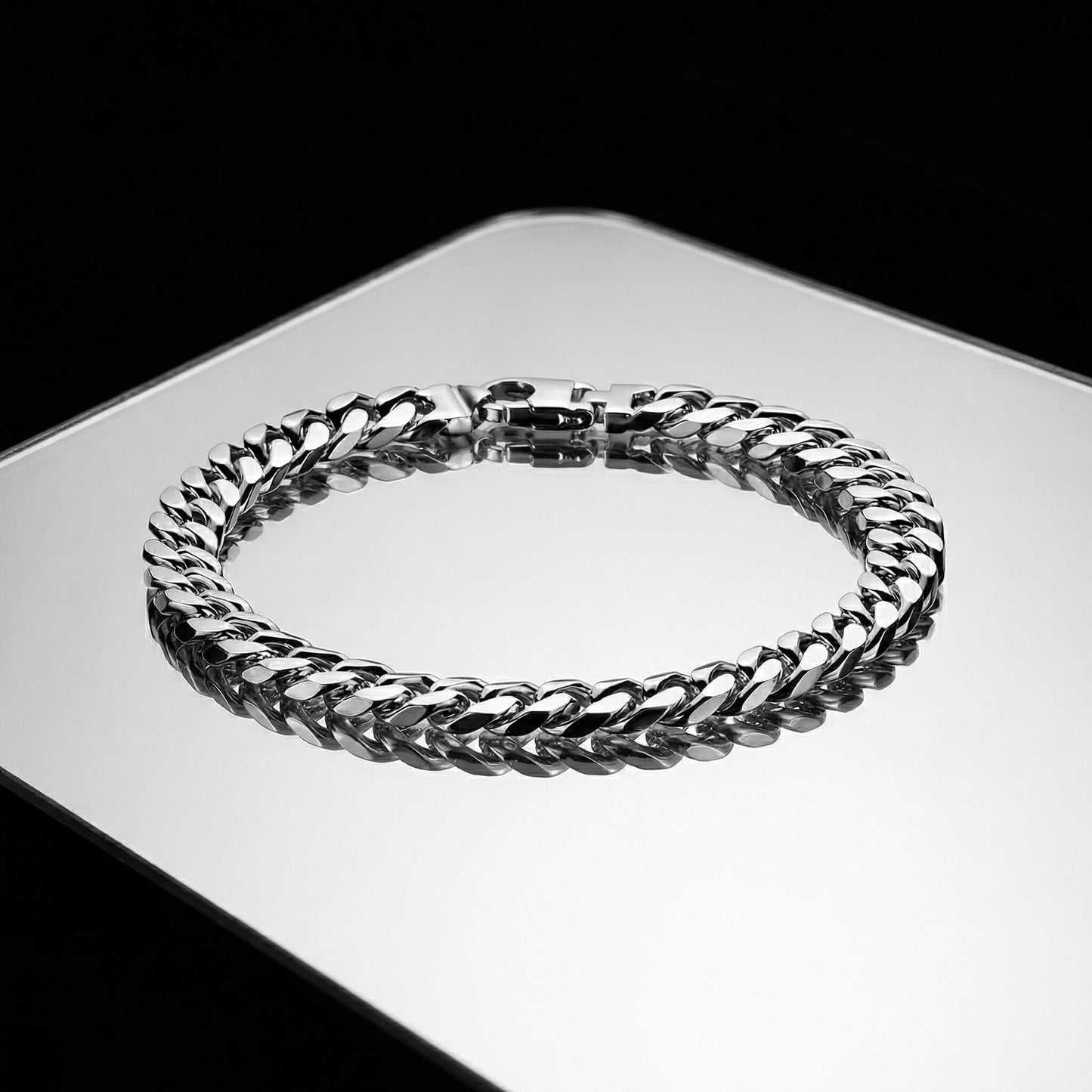 Silver bracelet with cuban links laying flat on a mirrored surface.