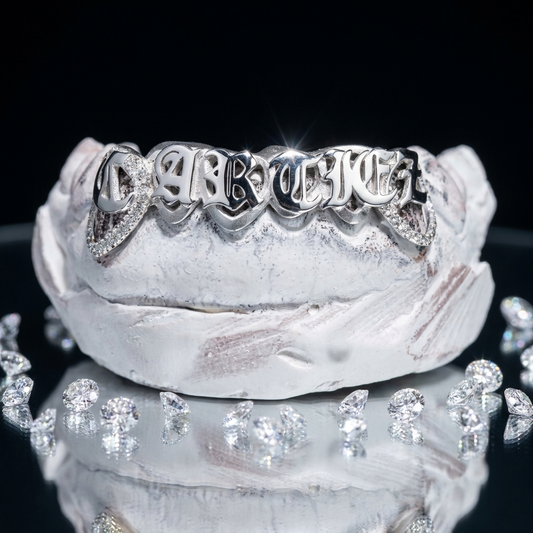 Luxury 14K white gold custom grillz featuring raised Old English lettering paired with pavé diamond canine window accents. Displayed on a dental mold with scattered loose diamonds.14K white gold custom grillz with raised Old English lettering and pavé diamond window ends on a dental model surrounded by brilliant-cut diamonds.