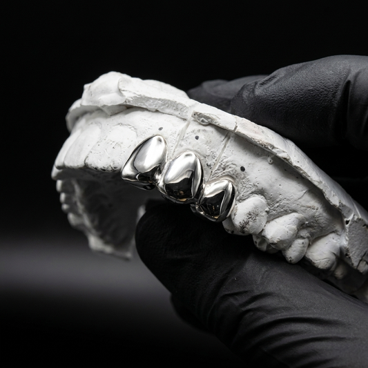 Sterling silver connected 3-piece full tooth cap grillz held on a white plaster dental mold over black silk.