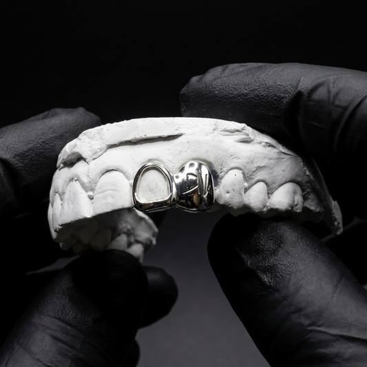 Polished 925 sterling silver custom grillz with custom engraved lettering on a solid tooth cap joined to an open cutout window on a dental mold.
