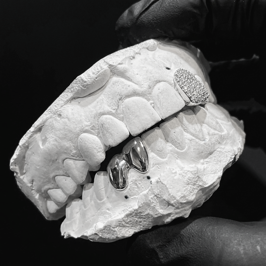 Sterling silver iced-out single diamond tooth cap and bottom 2-piece solid full caps displayed on a white dental cast.