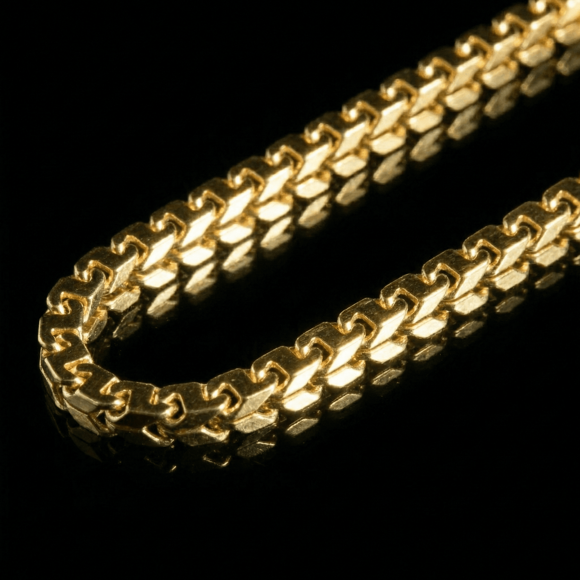 Clse up image of a yellow golden chain laying flat on a mirrored surface. The chain features links inspired by the figaro link.