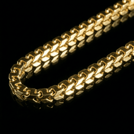Clse up image of a yellow golden chain laying flat on a mirrored surface. The chain features links inspired by the figaro link.