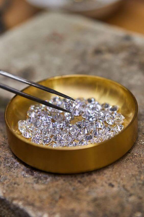 A golden cup with a pile of diamonds with a tweezer holding one of the diamonds.