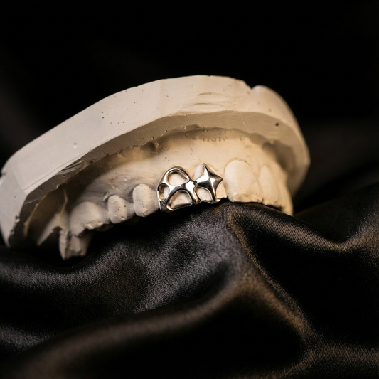 Silver grillz with a custom design fitted on a dental model. Laying on a black cloth.