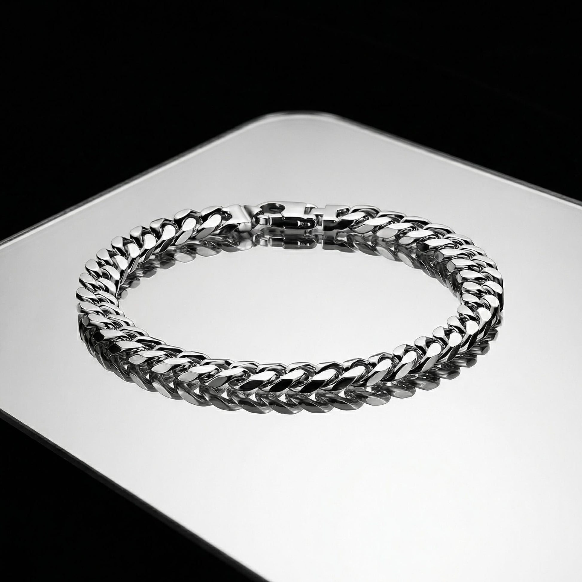 Silver bracelet with cuban links laying flat on a mirrored surface.
